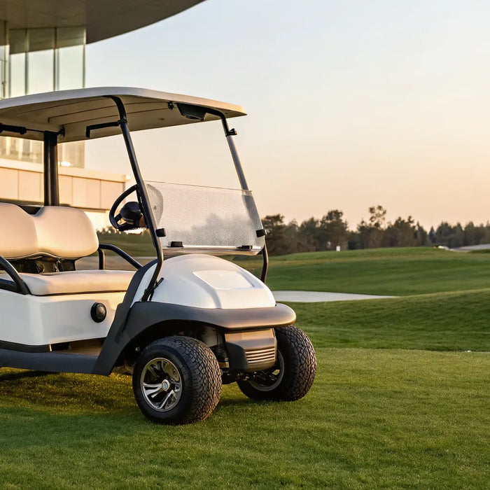 Club Car Precedent golf cart parked on grass near a modern clubhouse at sunset.