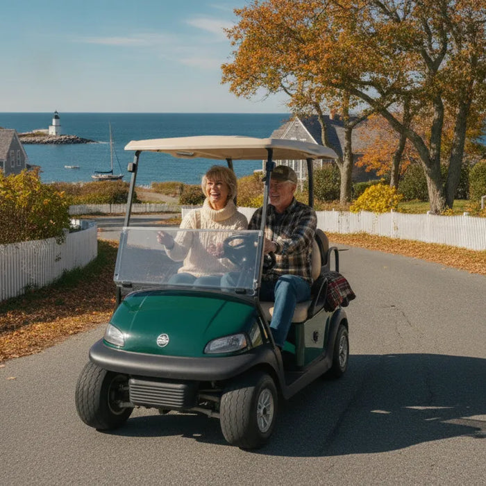 Active retirement couple driving a street-legal golf cart along a scenic New England coastal road in autumn